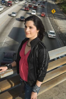 Side profile of a young woman standing on an overpass looking away