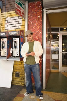 Young man using a mobile phone near a pay phone