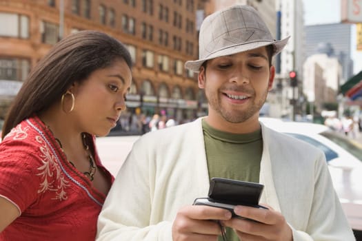 Close-up of a young man operating a personal data assistant with a young woman standing beside him