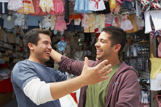 Close-up of two young men smiling in front of a clothing store