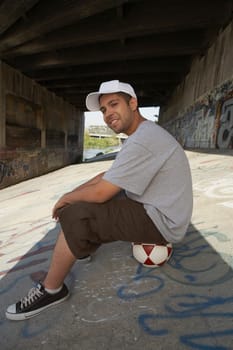 Side profile of a young man sitting on a soccer ball