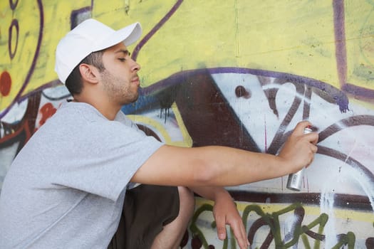 Side profile of a young man making a graffiti on a wall