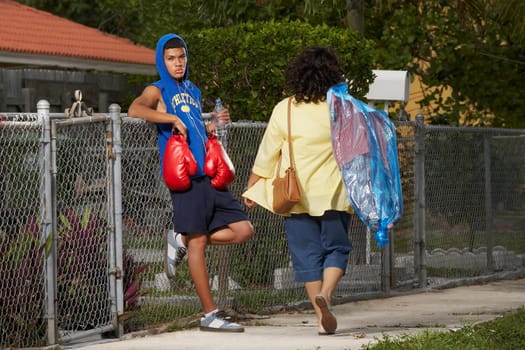 Rear view of a mature woman walking with a teenage boy leaning on a chain-link fence