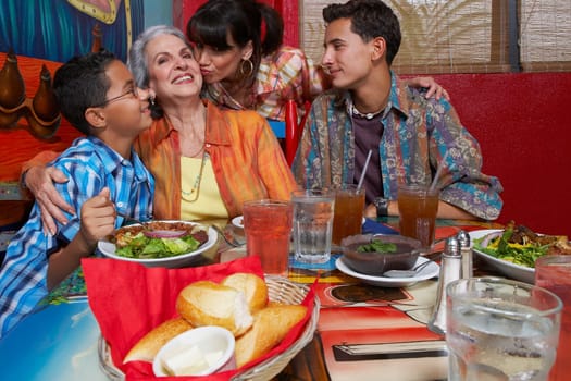 Mature woman kissing her mother with their two children sitting at a table in a restaurant
