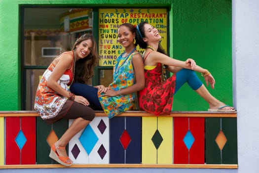 Three young women sitting on a railing and smiling