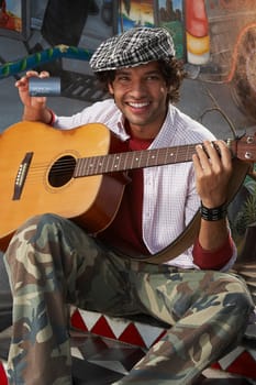 Portrait of a young man holding a guitar and a credit card