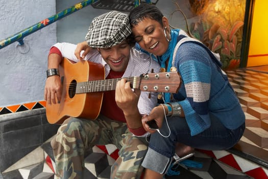 Young man playing a guitar and smiling with a young woman
