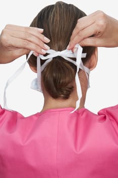 Rear view of a female nurse tying a surgical mask