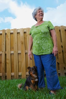 Low angle view of a senior woman standing with a dog in a lawn and smiling