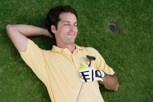 High angle view of a mid adult man lying on a golf course with a golf ball and a golf club