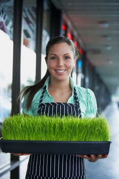 Portrait of a young woman holding a tray of wheatgrass and smiling