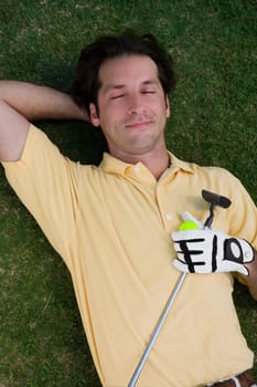 High angle view of a mid adult man lying on a golf course with a golf ball and a golf club