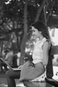 Side profile of a young woman sitting on a bench and using a laptop, Old San Juan, San Juan, Puerto Rico