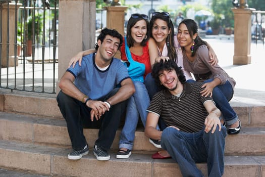 Two young men with three young women sitting on steps and smiling