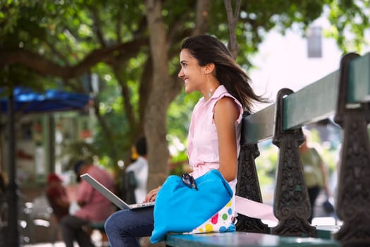 Side profile of a young woman sitting on a bench and using a laptop, Old San Juan, San Juan, Puerto Rico