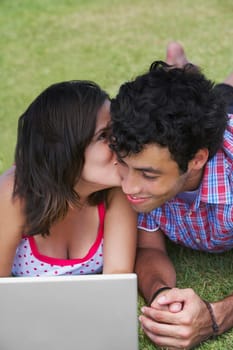 Close-up of a young couple lying in a lawn in front of a laptop