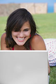 Close-up of a young woman lying in a lawn in front of a laptop
