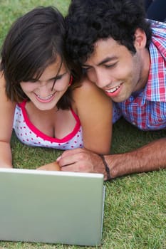 Close-up of a young couple lying in a lawn in front of a laptop