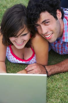Close-up of a young couple lying in a lawn in front of a laptop