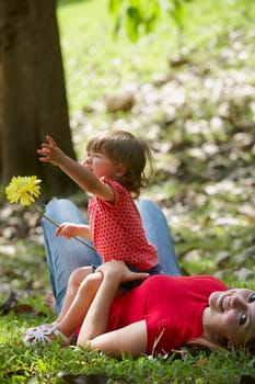 Portrait of a young woman lying on grass with her daughter sitting on her stomach