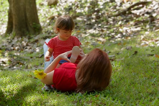 Young woman lying on grass with her daughter sitting on her stomach