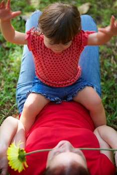 Young woman lying on grass with her daughter sitting on her stomach