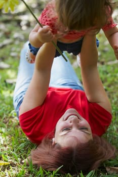 Young woman lying on grass and picking up her daughter