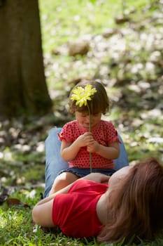 Young woman lying on grass with her daughter sitting on her stomach