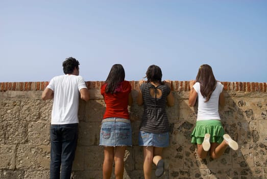 Rear view of three young women and a young man looking over a stone wall, Morro Castle, Old San Juan, San Juan, Puerto Rico