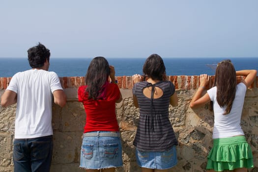 Rear view of three young women and a young man looking over a stone wall, Morro Castle, Old San Juan, San Juan, Puerto Rico