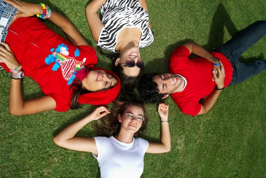 Three young women with a young man lying on grass and smiling