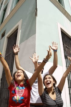 Two young women and a young man standing together with their arms raised and laughing