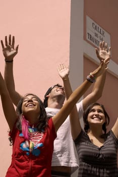 Two young women and a young man standing together with their arms raised and smiling