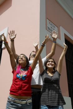 Two young women and a young man standing together with their arms raised and smiling