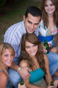 Young man sitting with three young women holding beer bottles and smiling