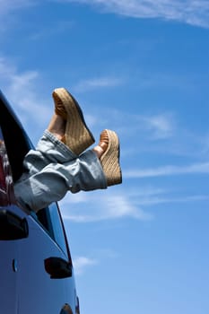 Low section view of a woman in a car with her legs outside the window