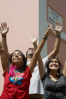 Two young women and a young man standing together with their arms raised and smiling