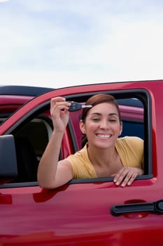 Portrait of a young woman leaning on the window of a car and showing a car key