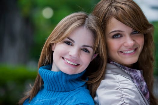 Portrait of two young women back to back and smiling