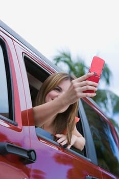 Young woman sitting in a car and taking a picture with a mobile phone