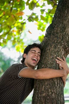 Young man hugging a tree trunk and laughing