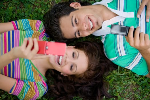 High angle view of a young couple lying in a park and holding mobile phones