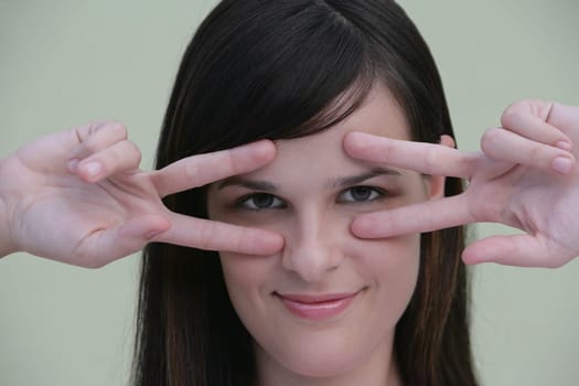 Portrait of a young woman making hand signs on her eyes and smiling