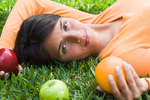 Teenage girl lying on grass and holding fruits