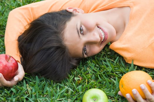 Teenage girl lying on grass and holding fruits
