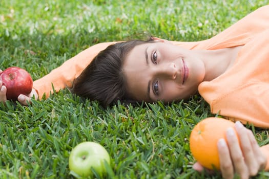 Teenage girl lying on grass and holding fruits