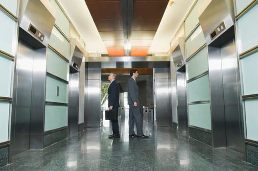 Businessmen standing back to back and waiting for elevators