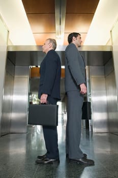Businessmen standing back to back and waiting for elevators