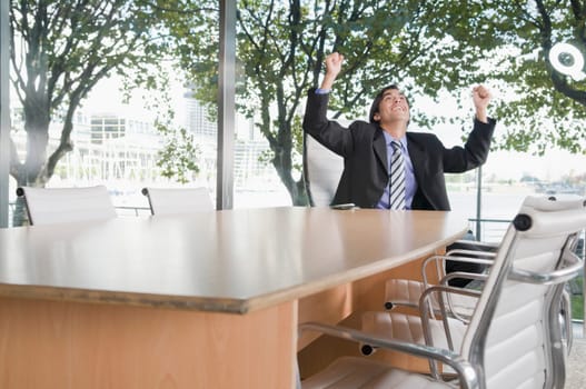 Businessman smiling with arms raised in a conference room