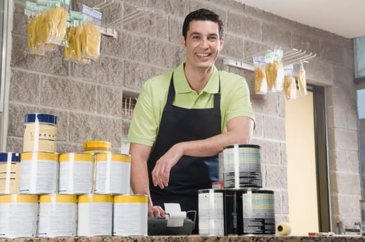Sales clerk standing at the counter of a paint shop and smiling